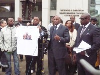 Carlton Berkeley of Brothers and Sisters Who Care holds a t-shirt with the faces of local leadership crossed out and the face of Kenneth Chamberlain Sr. as he was as a young Marine. The message on the shirt asks: “Who is the victim?” Speaking at the microphone is Kenneth Chamberlain, Jr. to his left is Damon Jones.