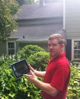 Kevin Singleton from Franzoso Contracting demonstrates the Roof Shampoo process on his iPad.  In the background is The Home Guru’s badly stained roof with mold and lichen, “before.”