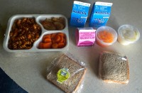 The daily meal delivery includes a freshly cooked hot meal, bread with butter, sandwich, milk, fruit juice, fruit cup and side salad or other accompaniment to the sandwich.
