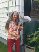 Councilwoman Milagros Lecuona with her dog Luke next to the rain barrel used to water the permeable driveway.