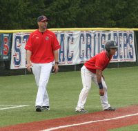 Stepinac Head Coach Keith Richardson (left), coaches third base, as Crusaders leadoff hitter Edwin Feliciano takes a lead. Richardson is in first year at the helm has Stepinac in First Place in their Division in the CHSAA AA. 
