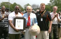 White Plains High School famed track star Dave Jackson (left), the only surviving member of the 1966 Tigers national record setting relay team, which included Larry James, Carl Reed and Otis Hill, joins his former Coach Ed Kehe (center), while presenting a plaque to White Plains Athletic Director Matthew Cameron, distinguishing the induction of the White Plains High School 1966 Mile Relay Team into the Penn Relays Wall of Fame this year. 