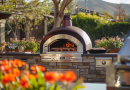 pizza oven buyers guide - photo of a beautiful backyard with red flowers and a pizza oven in the background next to a grill
