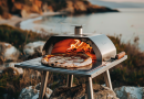 best portable pizza ovens - oven sitting on a rock which overlooks the serene rocky coastline of a lake