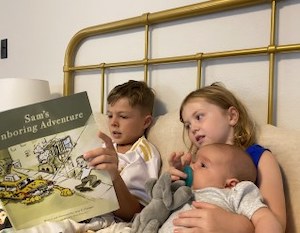 Three children in bed reading a book called "Sam's Unboring Adventure"