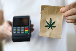 Individual holding a bag with a marijuana leaf on it and a credit card reader